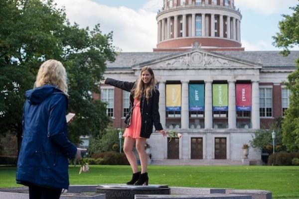 A young adult poses for a photo in front of 的 University of Rochester's Rush Rhees Library.